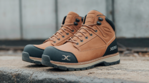 A pair of tan and black Xero Shoes, known for being comfortable work boots, rest on a concrete surface with a blurred background.