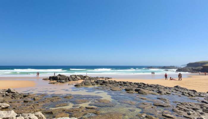 A sunny beach with clear waves, golden sands for sunbathing, rocky outcrops for exploration, accessible ramps, and diverse people enjoying the day under a bright blue sky.