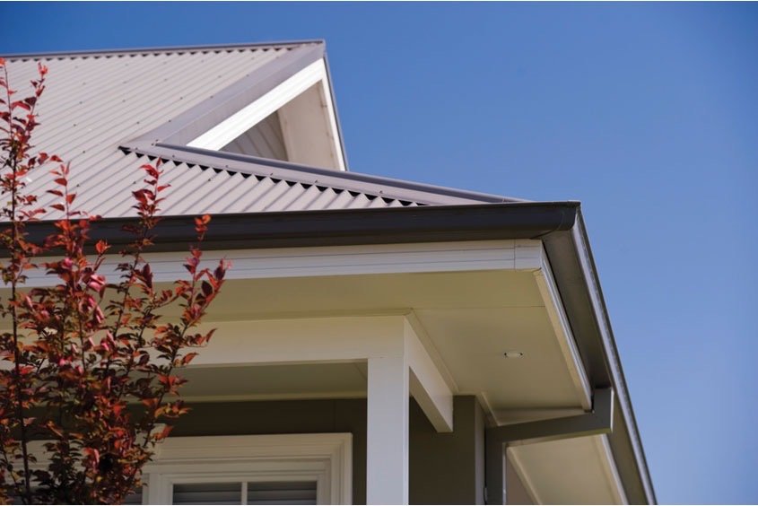 A light grey corrugated metal roof with a dark gutter and white eaves on a two-storey home